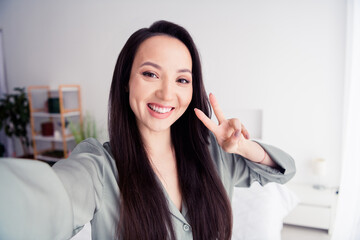 Photo portrait of attractive young woman toothy selfie photo show v-sign wear trendy gray pajama isolated on white modern interior design
