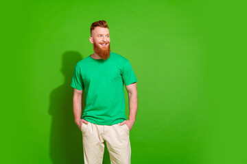 Fototapeta premium Portrait of good mood cool guy with long red beard wear stylish t-shirt look at promo empty space isolated on green color background