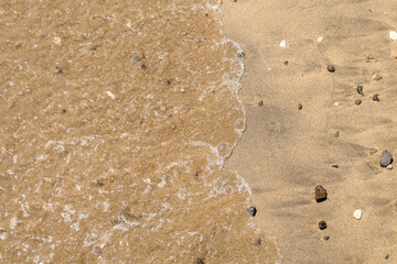 Ola y arena mojada por el efecto de las olas en la playa. Arena y pequeños cantos rodados arrastrado por la marea en la cala de Enmedio en Níjar, Almería, España. - obrazy, fototapety, plakaty