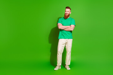 Full length photo of positive dreamy man dressed t-shirt arms folded looking empty space isolated green color background