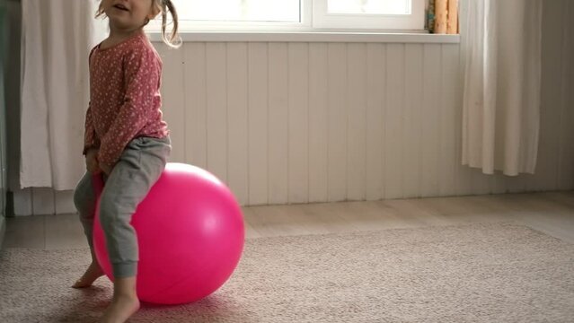 Space hopping child. Active fun. Happy kid jumping on bouncing ball. Bouncing on a Space Hopper. Childhood, leisure. Curly-haired funny girl plays on a large gymnastic ball, hoppity horses at home