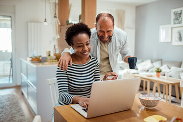 Diverse middle aged couple using laptop for online shopping at home