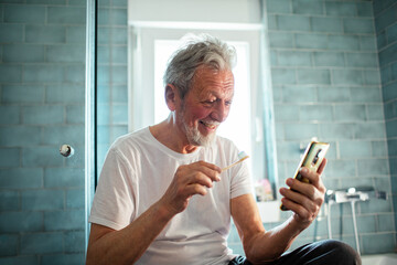 Smiling senior man using smartphone in bathroom