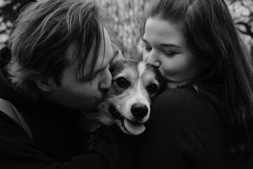 A young man and woman are kissing and hugging with their cute Welsh corgi puppy in the park. Dog...