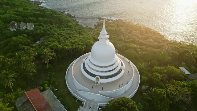 2023-03-15 - Unawatuna, Sri Lanka. Japanese Peace Pagoda. Aerial view of Buddhist pagoda on hill by ocean at sunset. Golden light bathes temple, peaceful, iconic spiritual site.