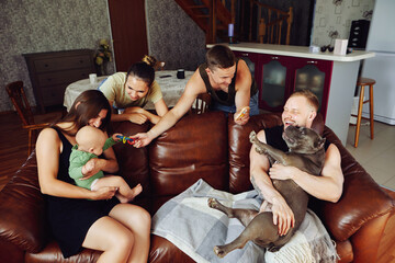 Young married couple with an American bully dog is sitting on sofa in living room while visiting...