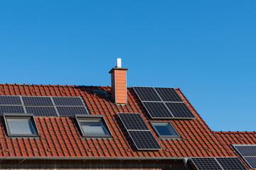 Tiled roof of a house with a chimney and solar panels under a blue sky.