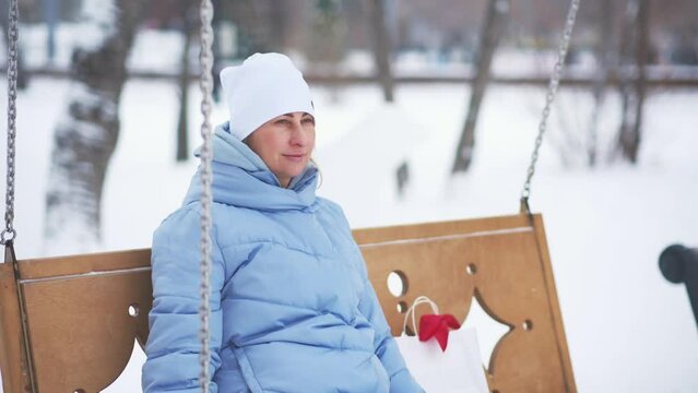 Young woman relaxing ang swinging on swings in winter in park near. 