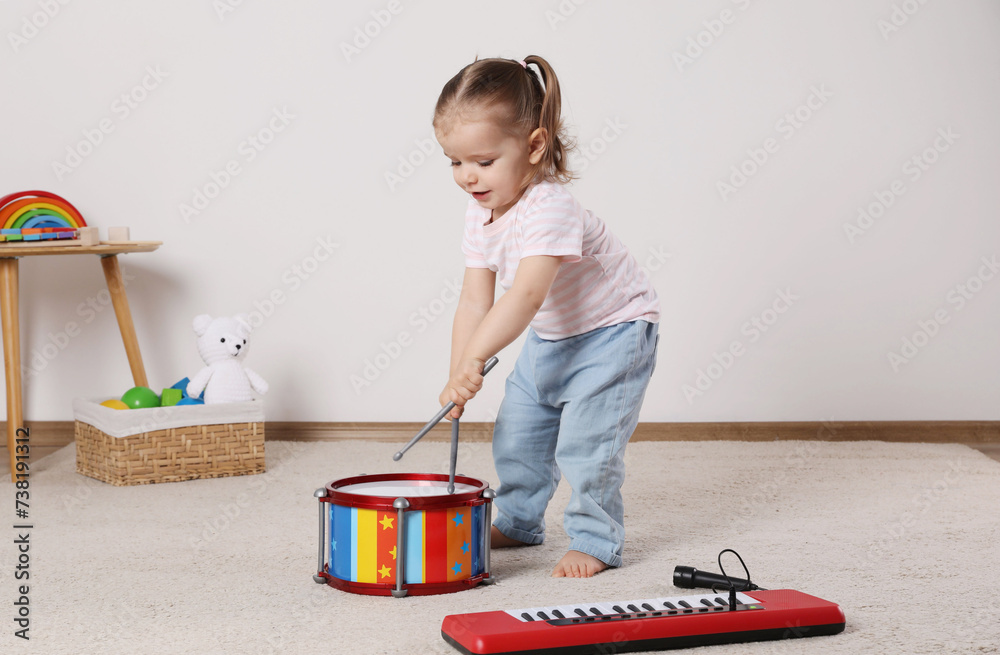 Wall mural Cute little girl playing with drum, drumsticks and toy piano at home