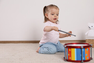 Cute little girl playing with drum and drumsticks at home, space for text