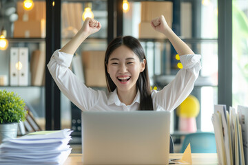 Happy excited young Japanese business woman accountant standing at the desk working on laptop...