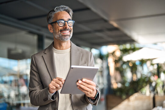 Happy elegant middle aged professional business man financial executive manager using digital tablet. Smiling confident mature businessman holding tab computer technology looking away at copy space.