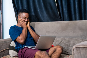 african man expressing happy feeling on the computer laptop screen with booth hands covering his...