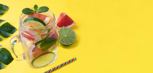 Detox or infused water with grapefruit and lime on the yellow background. Copy space. Close-up.
