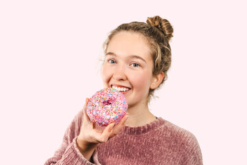 Happy young smiling woman looks at the camera and holds a delicious glazed donut in her hand...