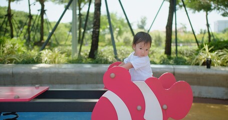 A young child enjoys a playful moment happily playing on a vibrant pink seesaw at a sunny park
