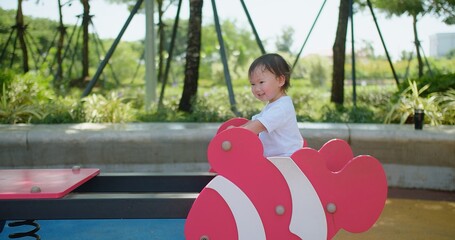 A young child enjoys a playful moment happily playing on a vibrant pink seesaw at a sunny park