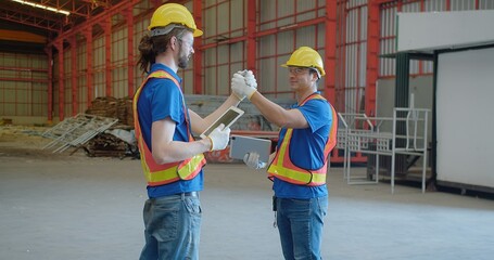 Two construction engineer workers in hard hats and vests engage in a friendly arm wrestling on a...