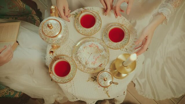 close up female hands take cup of tea golden porcelain service set. women noble sitting on sofa at coffee table have tea party fun. girl rest. woman queen royal room white vintage dress old style 4k