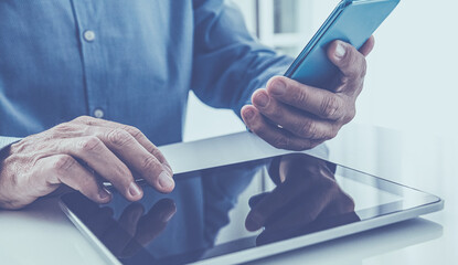 Closeup man hands using smartphone. Businessman works with tablet and mobile phone. Office workplace