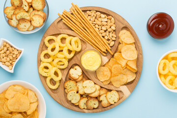 Board with unhealthy snacks on wooden background, top view