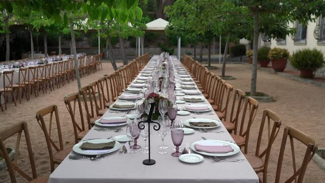 imagen est&aacute;tica de mesa alargada decorada, sillas de madera y arboles de fondo