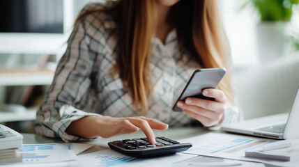 Fototapeta premium An economical woman diligently works on her phone calculator at home, efficiently managing bills and taxes online. She focused on financial planning, calculates expenditures and planning the budget