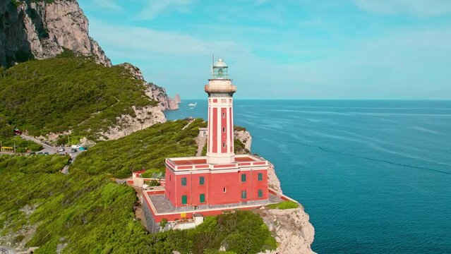 Capri coastline with lighthouse on rocky cliffs with green pine tree forest. Aerial view of Faro di Punta Carena in Italy.