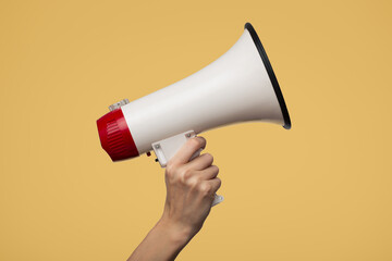 A hand holds a white megaphone. Yellow background.
