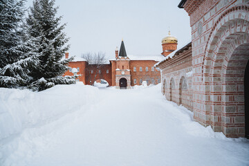 a snowy path leading to a brick building with a tower in the background