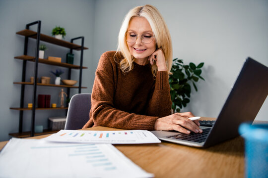 Photo of startup projects manager blond hair mature successful woman in brown sweater sitting desktop paperwork with money spends company