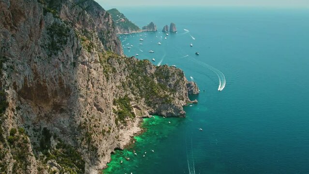 Breathtaking aerial view of Capri coastline with rugged cliffs. The ocean's hues of blue are sprinkled with vessels. Summer vacations in Italy.