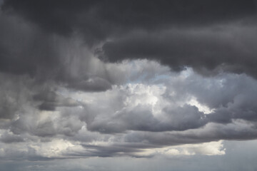 Grey storm clouds on a blue sky, rays of light on grey clouds