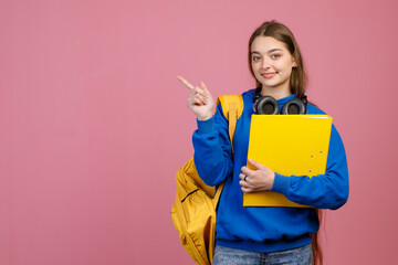  Happy female student standing, smiling, looking at camera. Glad, happy schoolgirl holding folder and rucksack, pointing by finger. Concept of youth lifestyle and education.