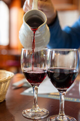 Pouring yound red beaujolais wine in glass during celebration of end of harvest and first sale release on third Thursday of November from white ceramic pitcher in Limouges, France
