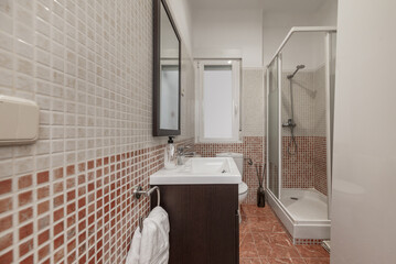 A small bathroom with stoneware-type tiles, dark wood furniture, mirror with matching frame, white...