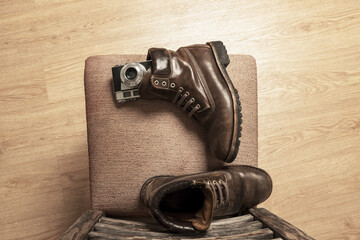 Brown leather boots next to a vintage camera on an upholstered chair viewed from the top