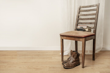 Brown leather hiking boots resting under a emaciated wooden chair with an old camera resting on the...