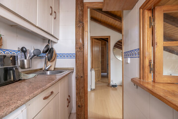 A small kitchen with wooden furniture and a serving hatch with a window to the living room