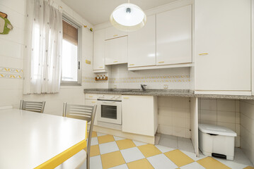 A kitchen with white wooden furniture, yellow details on the edge handles and white and yellow checkered floors