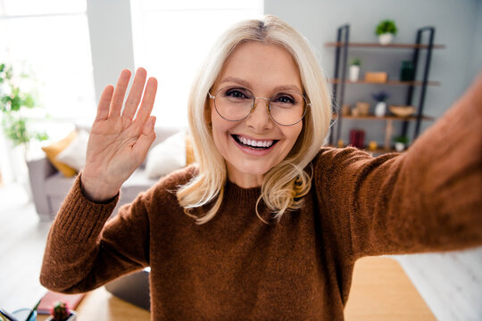 Selfie photo of pensioner cheerful business woman wear glasses in brown pullover waving hand for cadre sending greetings video content - Powered by Adobe