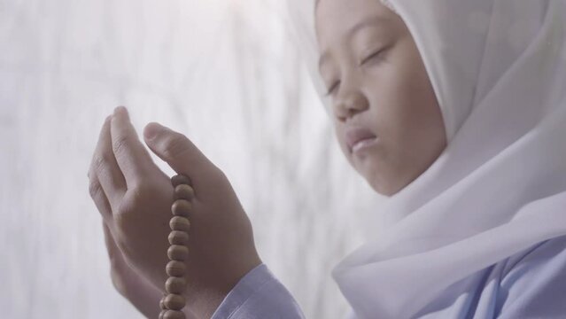 A little asian girl wearing hijab holds prayer beads while earnestly praying during the holy month of Ramadan
