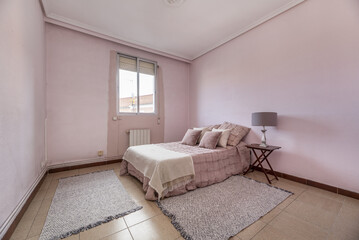 Room with a double bed with several fuchsia cushions, a matching bedspread, walls of the same color, twin rugs and an aluminum window without curtains