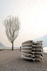 Stack up white paddle boards on a shore of lake Garda on a foggy day. Italy lago di Garda