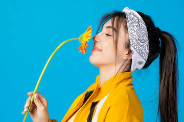 Side view of elegant, slim woman with hair band posing with long orange flower, smelling with...