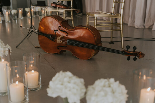 Violoncelo tumbado en el suelo. Hay velas y adornos florales delante. Detr&aacute;s hay dos sillas doradas con un violin encima de una de ellas.