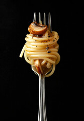 Minimal food concept, pasta, long spaghetti rolled on a fork on a black background, pasta fine dining.