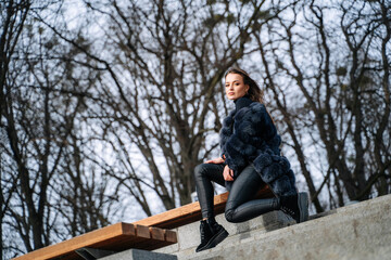 Fototapeta premium Young beautiful girl in blue coat sits on the steps in the park