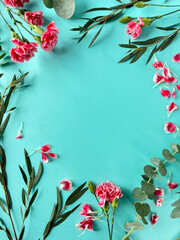 A photo featuring a blue background adorned with vibrant pink carnation flowers and lush green leaves, showcasing the natural beauty of this colorful composition. Copy-space on greeting card.