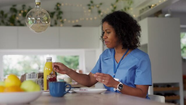Female nurse or doctor getting ready for work in the morning, eating breakfast and having cup of coffee, before leaving for the work dressed in scrubs. Work-life balance for healthcare worker.